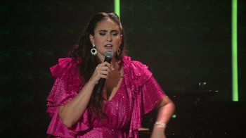 Movie still from “Catherine Cohen: The Twist...? She's Gorgeous” (2022), directed by Steven Brill – A woman in a pink dress is holding a microphone; Medium shot, Low angle