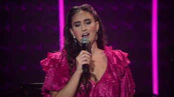 Movie still from “Catherine Cohen: The Twist...? She's Gorgeous” (2022), directed by Steven Brill – A woman in a pink dress is holding a microphone; Close Up shot, High angle