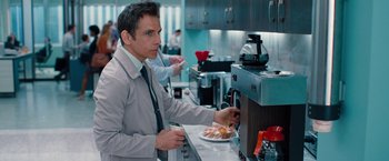 Movie still from “The Secret Life of Walter Mitty” (2013), directed by Ben Stiller – A man in a suit and tie eating food from a plate; Medium shot, Over the shoulder angle