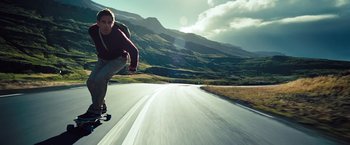 Movie still from “The Secret Life of Walter Mitty” (2013), directed by Ben Stiller – A man riding a skateboard down the side of a road; Wide shot, Low angle