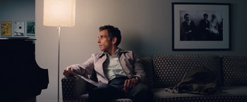 Movie still from “The Secret Life of Walter Mitty” (2013), directed by Ben Stiller – A man sitting on top of a couch in a living room; Medium shot, Over the shoulder angle