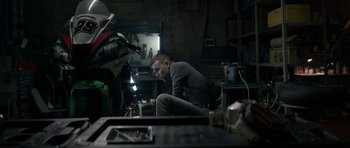 Movie still from “Centaur” (2022), directed by Daniel Calparsoro – A man sitting on the ground in a garage; Wide shot, Low angle