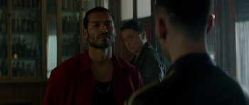 Movie still from “Centaur” (2022), directed by Daniel Calparsoro – A man looking at himself in the mirror while another man looks on; Medium shot, Over the shoulder angle