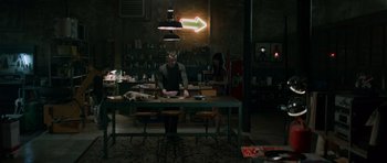 Movie still from “Centaur” (2022), directed by Daniel Calparsoro – A man sitting at a table in front of an arrow sign; Wide shot, High angle