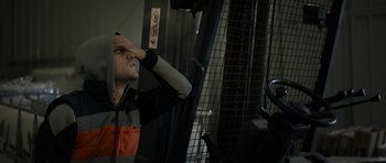 Movie still from “Centaur” (2022), directed by Daniel Calparsoro – A man standing next to a fork lift holding his hand to his face; Medium shot, Low angle