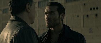 Movie still from “Centaur” (2022), directed by Daniel Calparsoro – A man standing next to another man in front of a building; Close Up shot, Over the shoulder angle