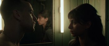 Movie still from “Centaur” (2022), directed by Daniel Calparsoro – A woman looking in the mirror with a man in the background; Close Up shot, Over the shoulder angle