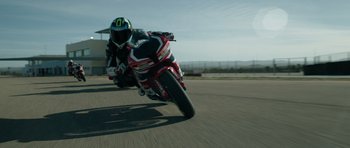 Movie still from “Centaur” (2022), directed by Daniel Calparsoro – A man riding a motorcycle down the middle of a race track; Extreme Wide shot, Low angle