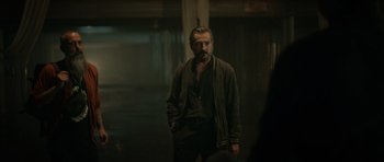 Movie still from “Centaur” (2022), directed by Daniel Calparsoro – A man standing in a room with his hands in his pockets; Medium shot, Over the shoulder angle