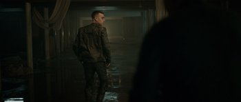 Movie still from “Centaur” (2022), directed by Daniel Calparsoro – A man standing in a dark room with a jacket on; Medium shot, Over the shoulder angle