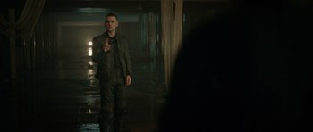 Movie still from “Centaur” (2022), directed by Daniel Calparsoro – A man standing in a dark room pointing to the ground; Medium shot, Over the shoulder angle