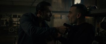 Movie still from “Centaur” (2022), directed by Daniel Calparsoro – A man is holding a gun in his hand and another man is holding a gun in his other hand; Close Up shot, Over the shoulder angle