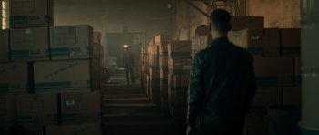 Movie still from “Centaur” (2022), directed by Daniel Calparsoro – A man standing in a room filled with stacks of cardboard boxes; Wide shot, High angle