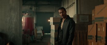 Movie still from “Centaur” (2022), directed by Daniel Calparsoro – A man standing in a room next to a bunch of boxes; Medium shot, Over the shoulder angle