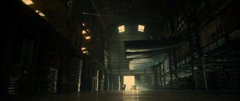 Movie still from “Centaur” (2022), directed by Daniel Calparsoro – A person standing in a large warehouse with a car; Extreme Wide shot, Low angle