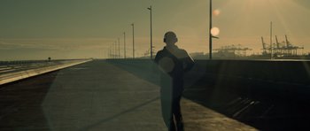 Movie still from “Centaur” (2022), directed by Daniel Calparsoro – A man standing on the side of a road with headphones on; Wide shot, Low angle