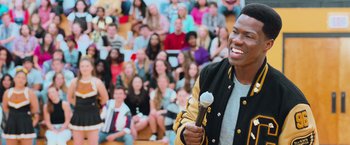 Movie still from “Central Intelligence” (2016), directed by Rawson Marshall Thurber – A man holding a microphone while standing in front of a group of people; Medium shot, Over the shoulder angle