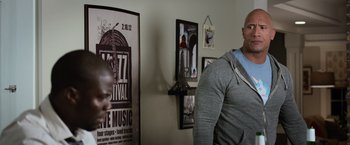 Movie still from “Central Intelligence” (2016), directed by Rawson Marshall Thurber – A man standing in front of a wall with posters on the wall; Medium shot, Over the shoulder angle