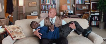 Movie still from “Central Intelligence” (2016), directed by Rawson Marshall Thurber – A man holding another man on a couch in a living room; Medium shot, Overhead angle