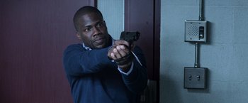 Movie still from “Central Intelligence” (2016), directed by Rawson Marshall Thurber – A man holding a gun in a room; Medium shot, Over the shoulder angle