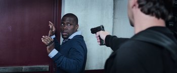 Movie still from “Central Intelligence” (2016), directed by Rawson Marshall Thurber – A man holding a gun in front of another man in a room; Medium shot, Over the shoulder angle