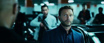 Movie still from “Central Intelligence” (2016), directed by Rawson Marshall Thurber – A man in a suit and tie holding a gun in front of another man in a suit and tie; Close Up shot, Over the shoulder angle