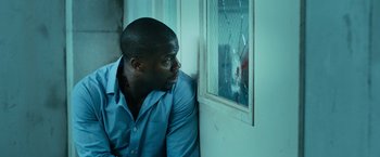 Movie still from “Central Intelligence” (2016), directed by Rawson Marshall Thurber – A man leaning against a wall looking out a window; Close Up shot, Over the shoulder angle