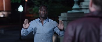 Movie still from “Central Intelligence” (2016), directed by Rawson Marshall Thurber – A man in a blue shirt holding his hand up; Medium shot, Over the shoulder angle