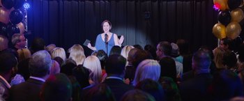 Movie still from “Central Intelligence” (2016), directed by Rawson Marshall Thurber – A woman standing at a microphone in front of a crowd; Wide shot, Over the shoulder angle
