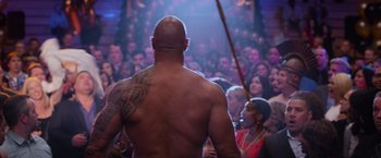 Movie still from “Central Intelligence” (2016), directed by Rawson Marshall Thurber – A man with a tattoo on his back standing in front of a crowd of onlookers; Medium shot, Over the shoulder angle