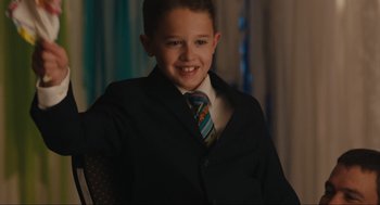 Movie still from “Cha Cha Real Smooth” (2022), directed by Cooper Raiff – A boy in a suit and tie smiling for the camera; Medium shot, Over the shoulder angle