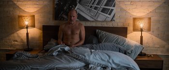 Movie still from “Champions” (2023), directed by Bobby Farrelly – A man sitting on a bed in front of a picture of a building; Medium shot, High angle