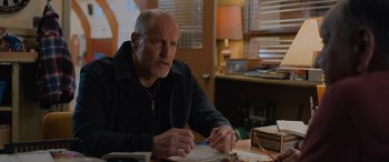 Movie still from “Champions” (2023), directed by Bobby Farrelly – An older man sitting at a table writing on a piece of paper; Medium shot, Over the shoulder angle