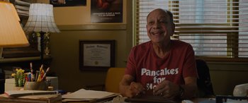 Movie still from “Champions” (2023), directed by Bobby Farrelly – An older man sitting at a table with papers in front of him; Medium shot, Low angle