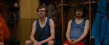 Movie still from “Champions” (2023), directed by Bobby Farrelly – A man and a woman sitting next to each other in front of a locker room; Medium shot, High angle