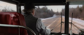 Movie still from “Champions” (2023), directed by Bobby Farrelly – An older man riding a bus on the side of a road; Medium shot, Over the shoulder angle
