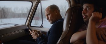Movie still from “Champions” (2023), directed by Bobby Farrelly – A man sitting in the back seat of a car looking at his cell phone; Medium shot, Over the shoulder angle