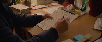 Movie still from “Champions” (2023), directed by Bobby Farrelly – A person writing on a paper on top of a wooden table; Close Up shot, High angle