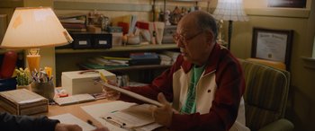 Movie still from “Champions” (2023), directed by Bobby Farrelly – An older man sitting at a table looking at papers; Medium shot, Over the shoulder angle
