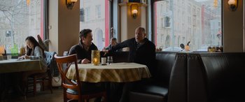 Movie still from “Champions” (2023), directed by Bobby Farrelly – Two men sitting at a table in front of a window; Medium shot, Over the shoulder angle