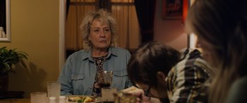 Movie still from “Champions” (2023), directed by Bobby Farrelly – An older woman sitting at a table with a glass of wine in front of her; Medium shot, Over the shoulder angle