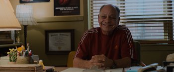 Movie still from “Champions” (2023), directed by Bobby Farrelly – An older man sitting at a table smiling for the camera; Close Up shot, Low angle