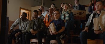 Movie still from “Champions” (2023), directed by Bobby Farrelly – A group of people sitting in a room watching a game; Medium shot, Low angle
