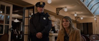 Movie still from “Champions” (2023), directed by Bobby Farrelly – A police officer standing next to a woman in front of a fireplace; Medium shot, Over the shoulder angle