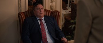 Movie still from “Champions” (2023), directed by Bobby Farrelly – A man in a suit and tie sitting in a chair; Close Up shot, Over the shoulder angle