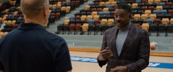 Movie still from “Champions” (2023), directed by Bobby Farrelly – A man in a suit talking to another man in a suit in an arena; Medium shot, Over the shoulder angle