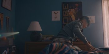 Movie still from “Chang Can Dunk” (2023), directed by Jingyi Shao – A person laying on a bed in a room with blue walls; Medium shot, Low angle