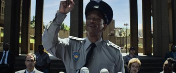 Movie still from “Chappie” (2015), directed by Neill Blomkamp – A man in a police uniform talking into microphones; Close Up shot, Low angle