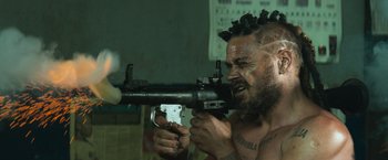 Movie still from “Chappie” (2015), directed by Neill Blomkamp – A man with dreadlocks holding a machine gun in his hands; Close Up shot, Low angle