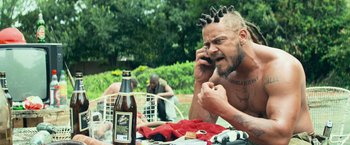 Movie still from “Chappie” (2015), directed by Neill Blomkamp – A man sitting at a picnic table talking on a phone; Medium shot, Low angle